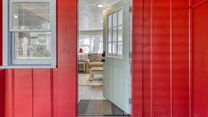 A red exterior with a white door leading to a room with a beige sofa and a small table. - Little Palm Hideaway Cottage (St. Augustine)