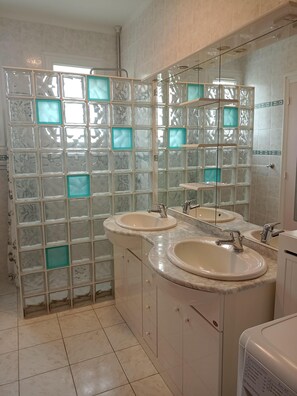Une salle de bain avec deux lavabos, une douche à parois de verre et un grand miroir.