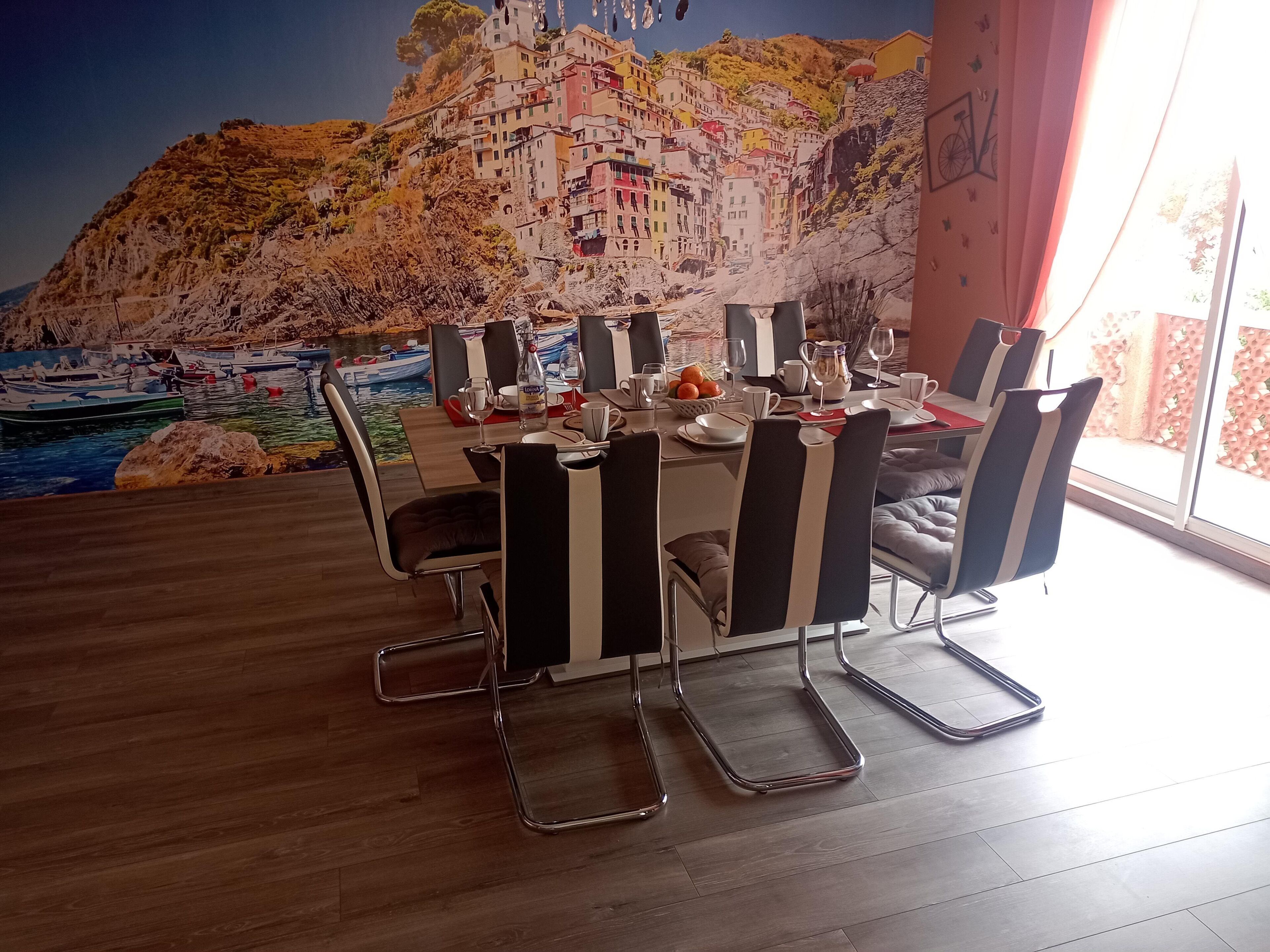 A dining area with a mural of a coastal village, a table set for four, and modern chairs.