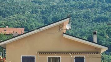 Un edificio a un piano con tetto spiovente, un'antenna parabolica e un camino. È circondato da vegetazione lussureggiante e montagne sullo sfondo.