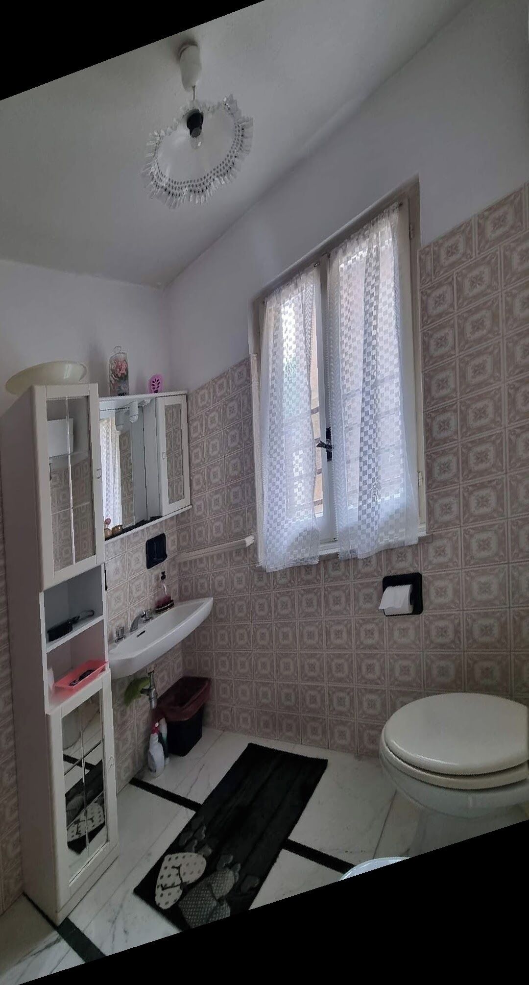 A bathroom with a white sink, a mirror, a toilet, and patterned wallpaper.
