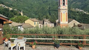 A rustic village with a prominent church tower, paved patio with chairs, and lush green hills in the background. - La Casa Di Edy (Prato)