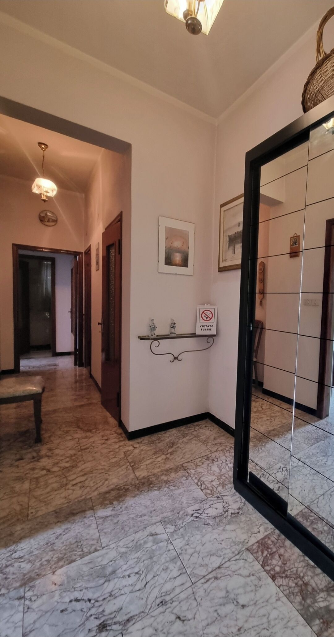 Un corridoio con pavimento in marmo, una panca, una mensola a parete con un cartello ‘no smoking’ e un quadro incorniciato.