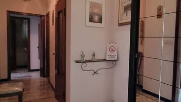Un corridoio con pavimento in marmo, una panca, una mensola a parete con un cartello ‘no smoking’ e un quadro incorniciato.