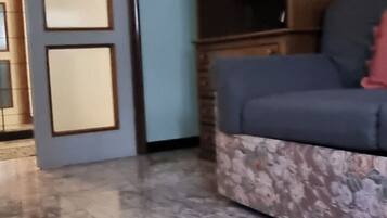 Ein Wohnzimmer mit Marmorboden, einer mit Blumenmuster bezogenen Couch und einer Holzkabine mit Glastüren.