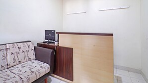 Ein kleiner, sauberer Raum mit einem Holztisch, einem Computer und einem gepolsterten Sofa mit Muster.