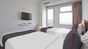 Ein Hotelzimmer mit zwei Betten, einem Fernseher, einer Klimaanlage, einem Fenster mit Vorhängen und einem Balkon.