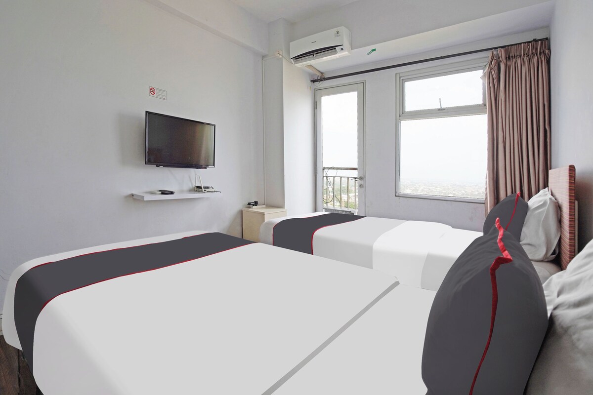 Een hotelkamer met twee bedden, een televisie, een airconditioner, een raam met gordijnen en een balkon.