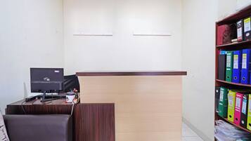 A reception desk with a computer, a chair, and a bookshelf with binders.