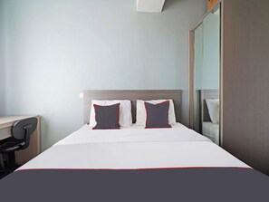 Una habitación de hotel con una cama, dos almohadas, un escritorio y un espejo.