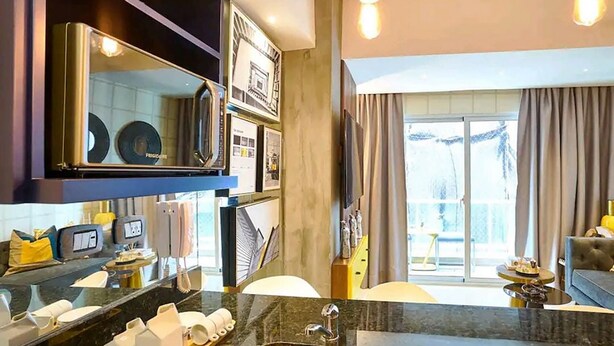 A modern hotel room with a kitchen area, a large mirror, and a balcony with curtains.