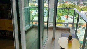 A balcony with a glass door, a small round table with a potted plant, and a cushioned bench.