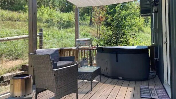 Una terraza techada al aire libre con un jacuzzi, una parrilla y una silla de mimbre.