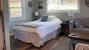 Un dormitorio con una cama, dos mesitas de noche, una silla y un ventanal.