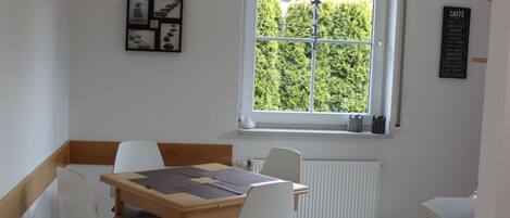 A dining area with a table and chairs, a window with a view of greenery, and a wall with a menu board.