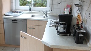 Una cocina con lavavajillas, cafetera y ventana con vistas al verdor.