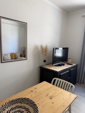 Una habitación con una mesa de comedor de madera, un televisor sobre un mueble de madera, un espejo en la pared y un jarrón con plumas de pluma.