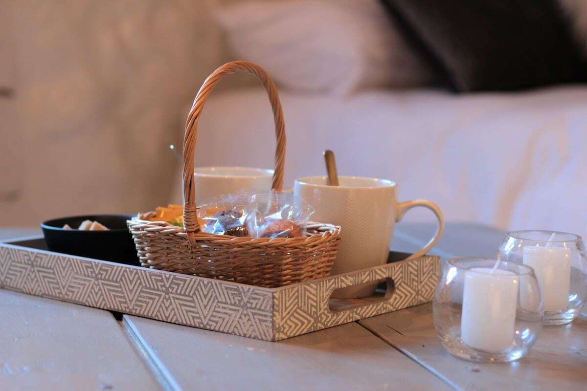 A tray with a wicker basket, a white mug, and two glass candles on a tiled surface.