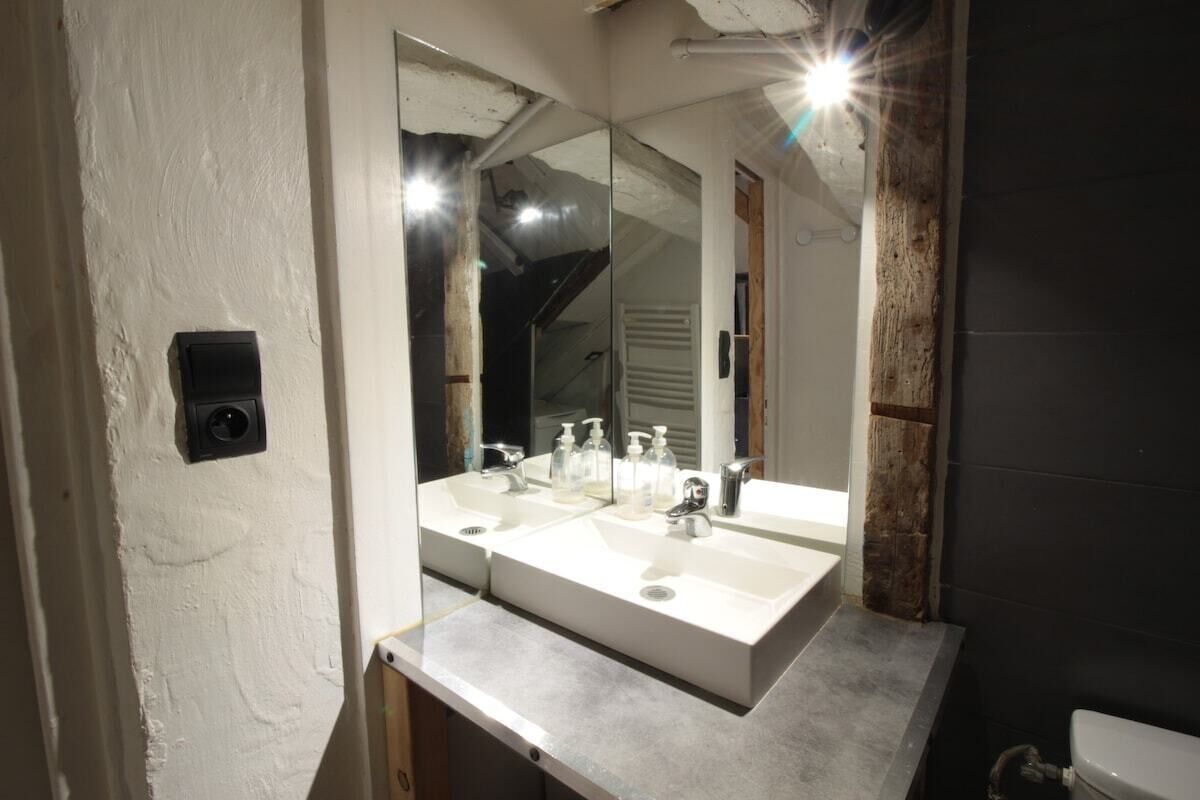 A bathroom with a white sink, two faucets, and a large mirror.