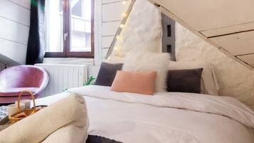 A cozy bedroom with a sloped ceiling, a bed with white bedding, a fluffy pillow, and a pink chair.