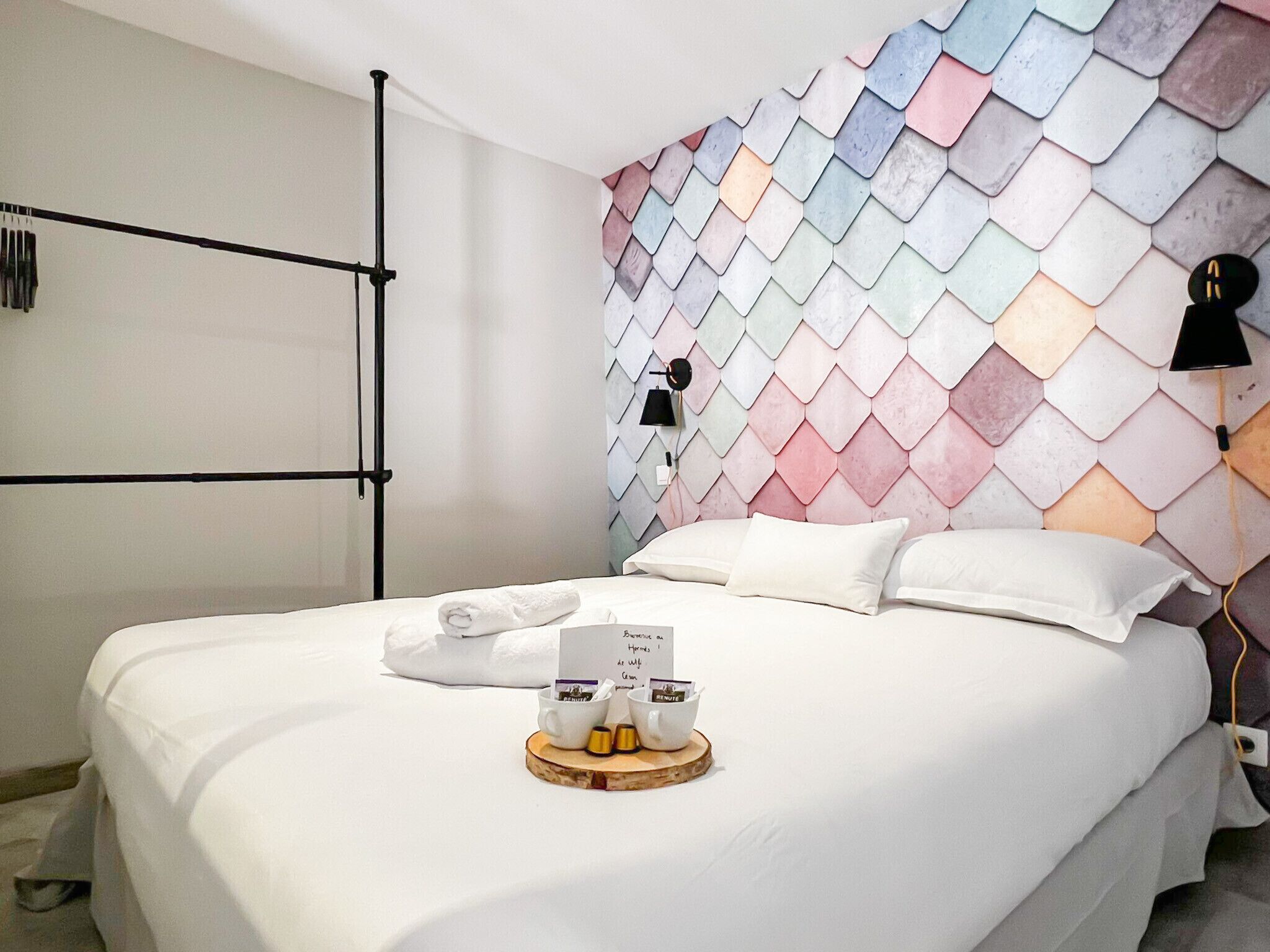 Een hotelkamer met een bed, een handdoek, een dienblad met een koffiekopje en een muur met een geometrisch patroon.