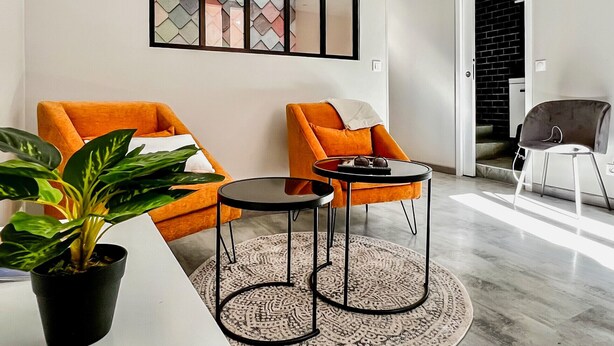 Una sala de estar moderna con dos sillones naranjas, una mesita redonda y una planta en maceta.