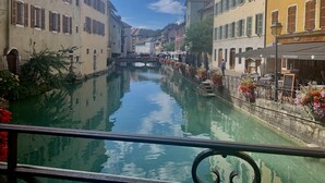 Un canal flanqueado por edificios, un puente a lo lejos y mesas al aire libre para un restaurante.
