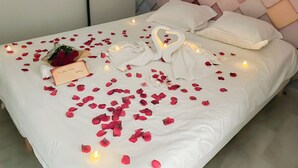 Una cama bien arreglada adornada con pétalos de rosa, velas y un detalle con forma de corazón.