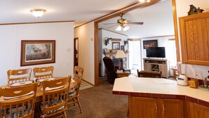 A dining area with wooden chairs and a table, a kitchen with wooden cabinets and a refrigerator, and a living room with a fireplace and a television.