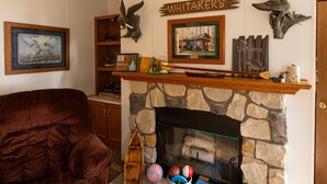 A cozy living room with a stone fireplace, a plush red armchair, and various decorative items including a sign reading "The Whitaker's".