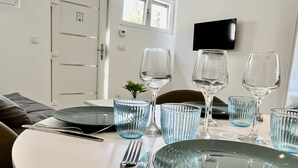 A dining table set with clear glassware and plates, a small plant, and a flat-screen TV mounted on the wall. - Leana t2 avec parking (Annecy)