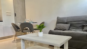 A modern living room with a grey sofa, a white coffee table, and a dining area with chairs and a table. - Leana t2 avec parking (Annecy)