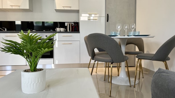 A modern kitchen with white cabinets, a built-in stove, and a dining area with a table and chairs. - Leana t2 avec parking (Annecy)
