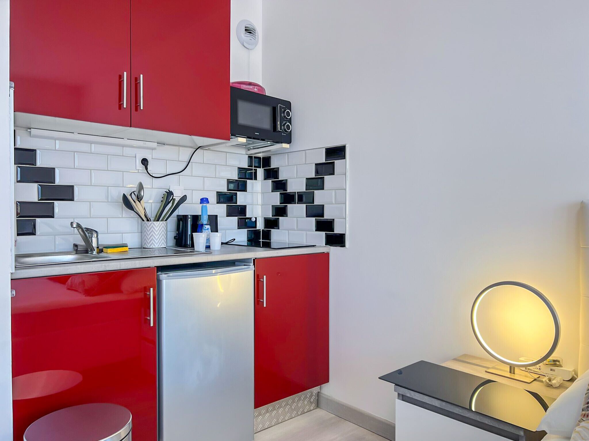 Une cuisine de taille réduite avec des meubles de couleur rouge, un four à micro-ondes et un petit réfrigérateur.