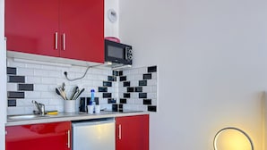 Una cocina compacta con armarios rojos, un microondas y un refrigerador pequeño.