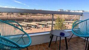 Un balcón con dos sillas turquesa y una mesa pequeña, con vista a una estación de autobuses.