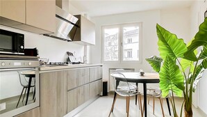 A modern kitchen with a stove, oven, and sink. There is a dining table with chairs and a large plant in the corner. - Marquis proche du centre ville (Annecy)