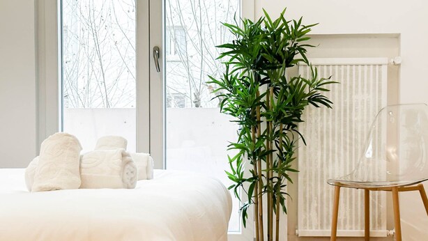 A bedroom with a bed, two rolled towels, a potted plant, a clear chair, and a radiator. - Marquis proche du centre ville (Annecy)