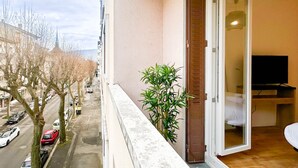 A balcony with a view of a street and parked cars, a potted plant, and an open door leading to a room with a bed and a TV. - Marquis proche du centre ville (Annecy)