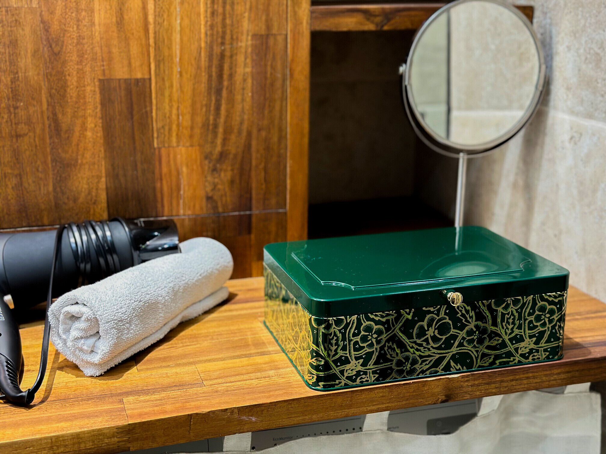 Un tocador de madera con una caja verde, una toalla blanca y un secador de pelo.