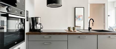 Una cocina moderna con horno empotrado, cafetera y lavabo con grifo.