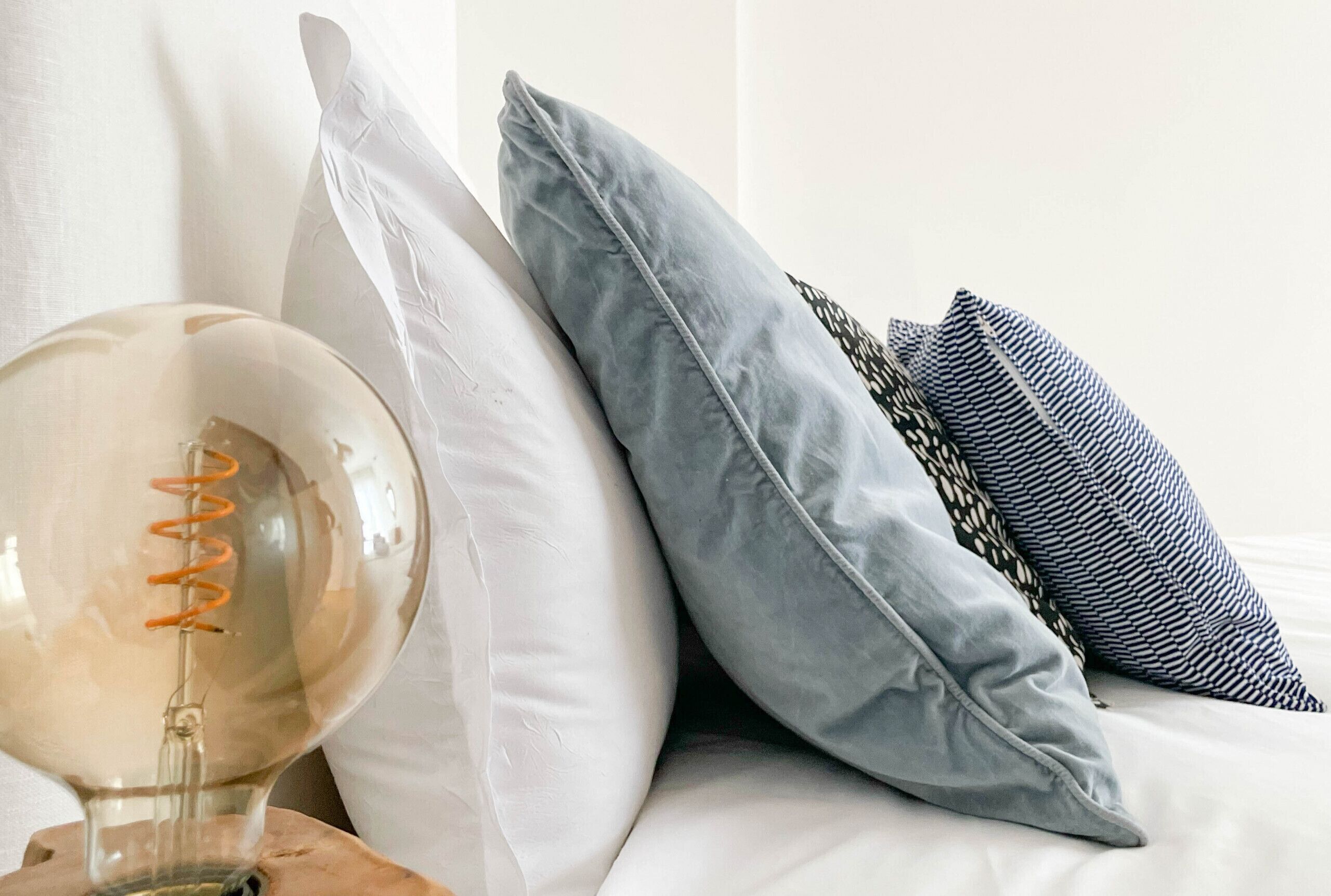 Una cama con una lámpara de vidrio transparente y varias almohadas.