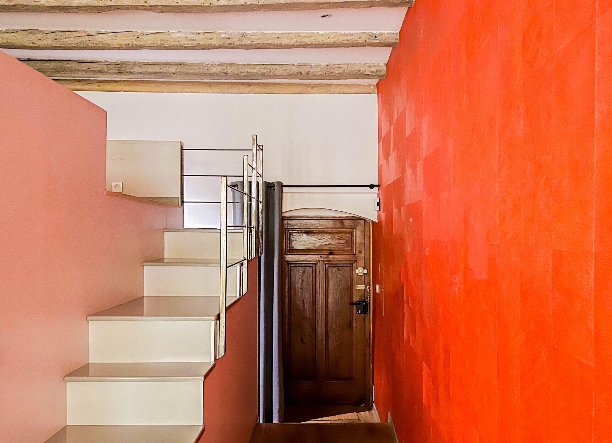 A staircase with white steps leading to a wooden door, a metal railing, and a red wall.