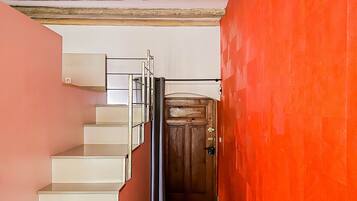 A staircase with white steps leading to a wooden door, a metal railing, and a red wall.