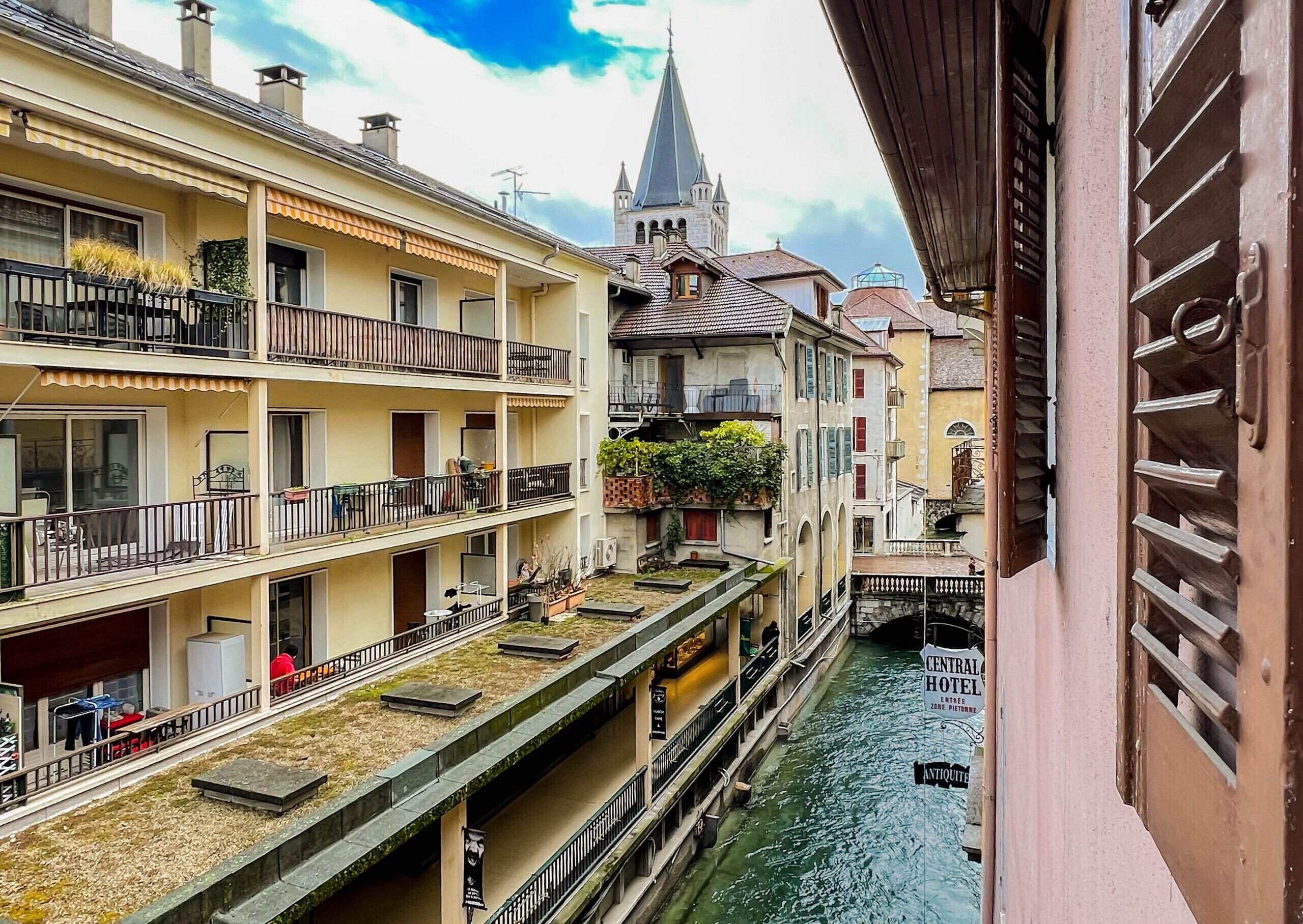 A canal-side building with multiple balconies, a church spire in the background, and a sign for the Central Hotel.