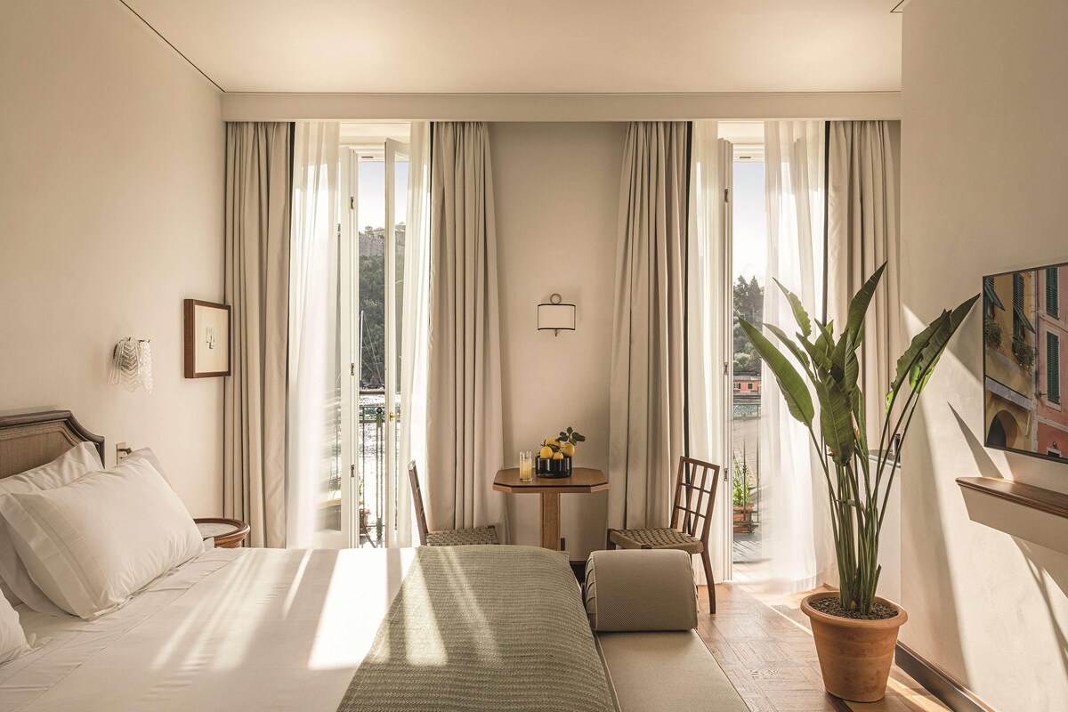 Une chambre d’hôtel avec un lit, une petite table sur laquelle se trouve un vase, une chaise et une plante en pot.