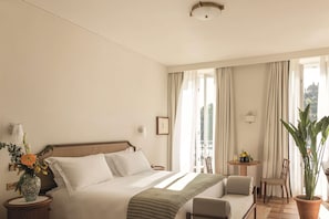 Une chambre d’hôtel avec un lit, une petite table et une chaise, une plante en pot et une vue sur l’extérieur.