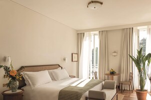 Una camera d'albergo con un letto, un tavolino con una sedia, una pianta in vaso e vista sull'esterno.