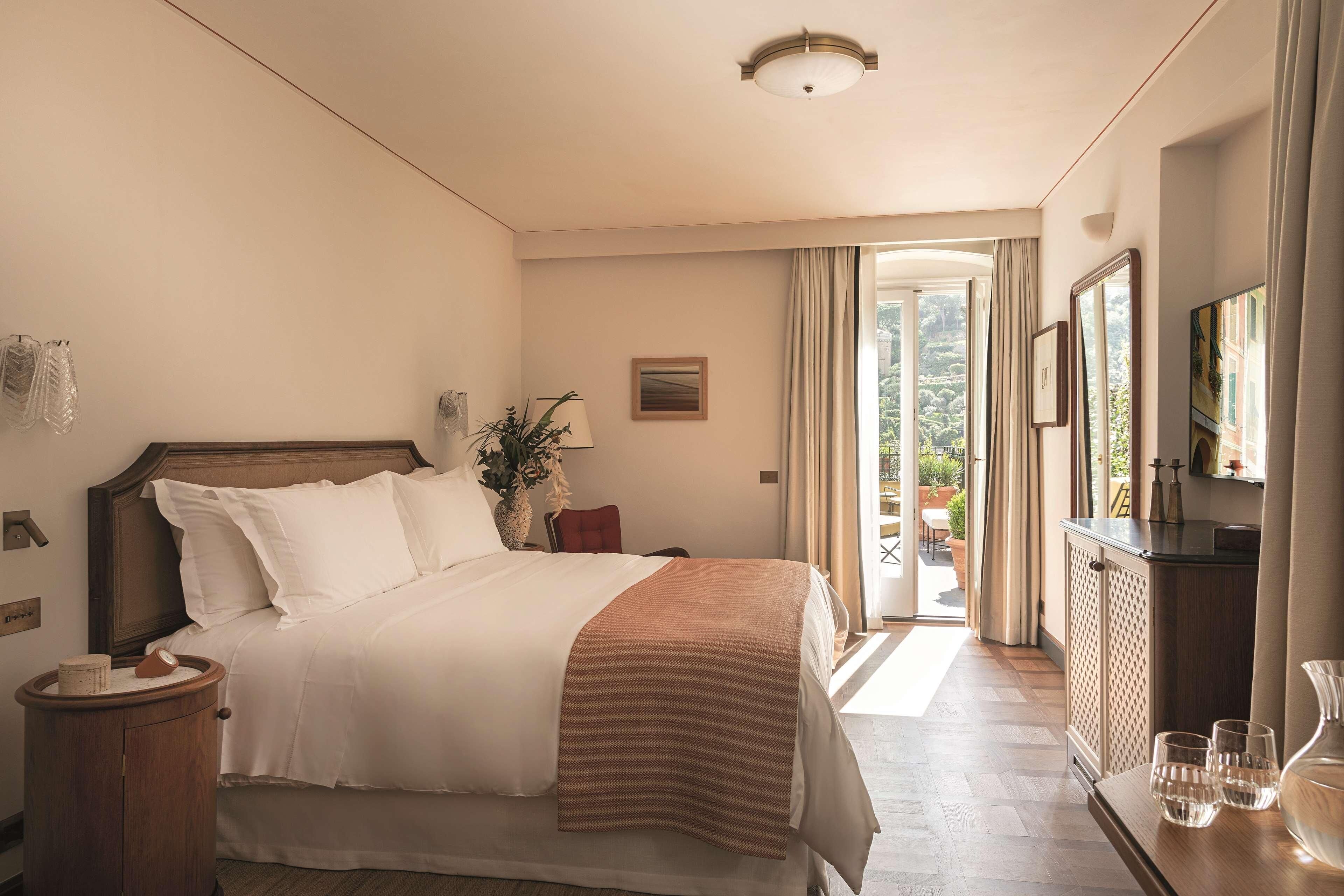 Quarto de hotel com uma cama grande, mesa de cabeceira, cômoda e vista para o exterior.
