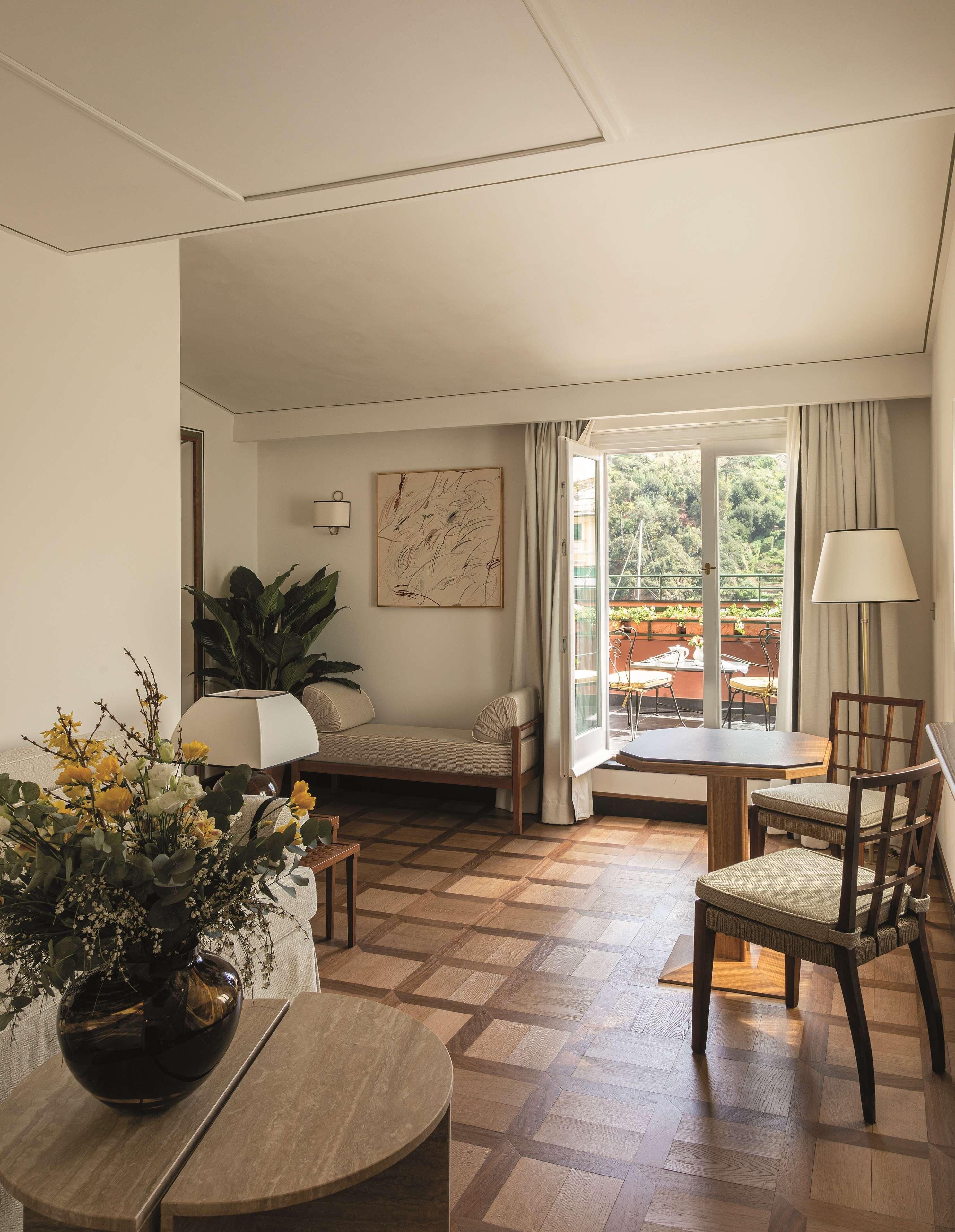 Una sala de estar acogedora con un sofá, una mesa de comedor y sillas. Hay una ventana con cortinas, una planta y un cuadro en la pared.